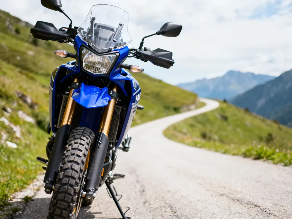 Niebieska Yamaha Tenere 700 na górskiej drodze, z przodu widoczne terenowe opony, w tle kręta trasa w zielonych wzgórzach.